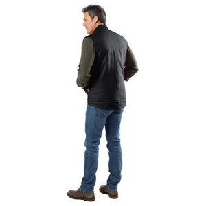 Man wearing a black vest over an olive green long sleeve shirt and blue jeans