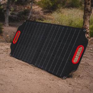 Foldable black solar panel with red handles standing on dirt ground