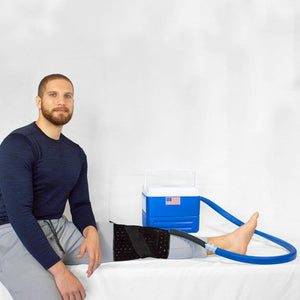 Man using a cold therapy knee wrap connected to a blue portable cooler