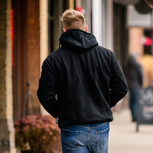 Person wearing a black hooded sweatshirt and blue jeans walking on a sidewalk