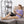 Woman sitting on a sofa using a black electric knee heating pad while looking at a smartphone