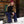 Woman with long hair wearing a red beanie and black jacket sitting on a stone pillar in the snow