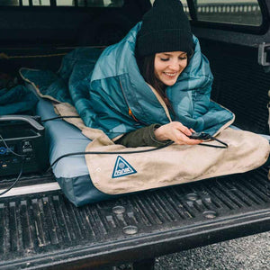 Person in a sleeping bag using an Ignik heated blanket in the back of a truck
