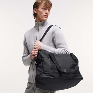 Person wearing a grey zip sweater carrying a black Got Bag duffel bag