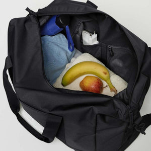 Open black Got Bag duffel containing a towel, banana, apple, umbrella, and charger