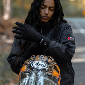 Person wearing Venture Heat black heated gloves with power button visible near wrist and an Arai motorcycle helmet