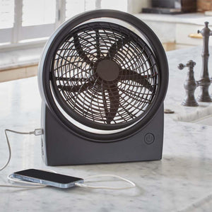 Black portable desk fan charging a smartphone on a marble countertop