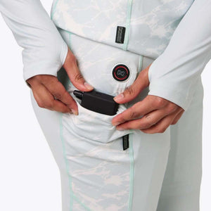 Hands placing a black Mobile Warming battery pack into a pocket on light blue patterned thermal leggings