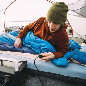 Person in a tent using a portable power station to control a heated sleeping bag