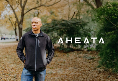 A bald man in a black zip-up jacket and blue jeans stands left in an autumn park. White text 
