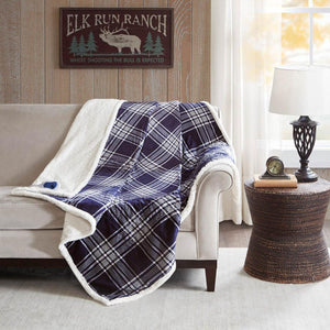 Woolrich navy plaid heated throw blanket with white sherpa lining draped over a beige sofa