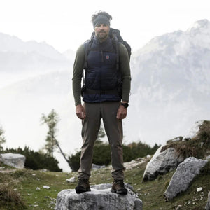 Man wearing FjallRaven vest and hiking gear standing on a rock in the mountains