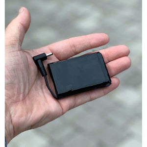 Small black rectangular battery pack with a short power connector cable held in a palm