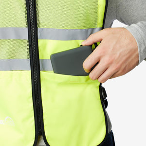 Hand placing a grey rectangular device into the pocket of a high visibility neon yellow safety vest
