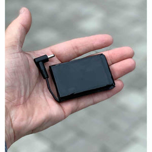 Small black rectangular battery pack with an L-shaped power connector held in a palm