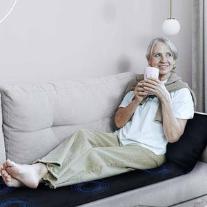 Woman sitting on a sofa using a UTK Technology infrared heating mat