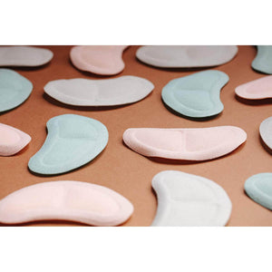 Assorted pink and mint green adhesive heel cushions on a brown background