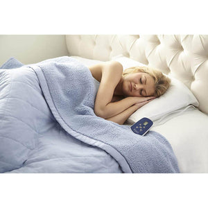 Person sleeping under a blue heated blanket with a digital controller on the bed