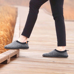 Person wearing grey wool slip on shoes with black soles on a wooden boardwalk