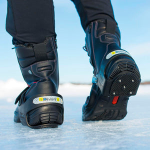 Person wearing black boots with Devisys ice cleats on snowy ground