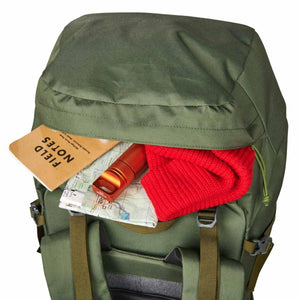 Kelty backpack top pocket containing a Field Notes notebook, a map, a flashlight, and a red knit hat
