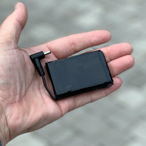 Small black rectangular battery pack with an L-shaped power connector held in a palm