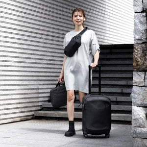Person wearing a Thule crossbody bag and carrying a Thule briefcase and rolling luggage