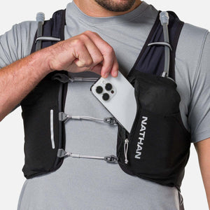 Person placing a smartphone into the front pocket of a black Nathan hydration vest