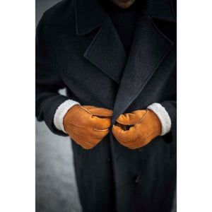 Person wearing Hestra tan suede gloves with white shearling cuffs and a dark wool coat
