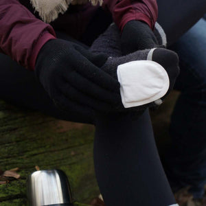 Person wearing black gloves applying a white adhesive toe warmer to a grey wool sock