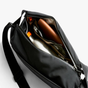 Open Bellroy black sling bag showing internal compartments with a water bottle and accessories