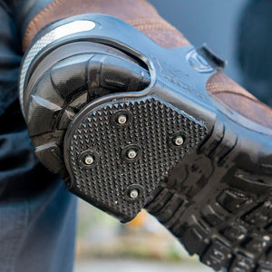 Black rubber heel traction device with metal spikes attached to a brown leather boot
