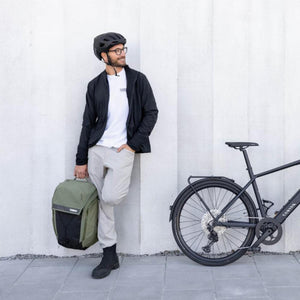 Man wearing a helmet holding a green Thule backpack next to a bicycle