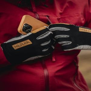 Person wearing Hestra gloves placing a smartphone into a red jacket pocket