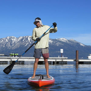 Person wearing Glacier Glove apparel paddle boarding on a lake with mountains in the background