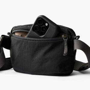 Black Bellroy sling bag with a smartphone partially inside the front zipper pocket
