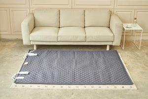 Grey quilted electric heating mat on a beige rug in front of a beige sofa
