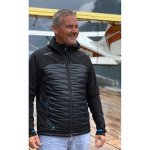 Man wearing a black Volt hooded jacket standing on a wooden dock with a seaplane in the background