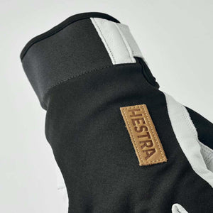 Close up of black and white Hestra glove with leather brand patch