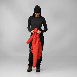 Person wearing black long sleeve shirt, black beanie, and black trousers holding a red quilted jacket