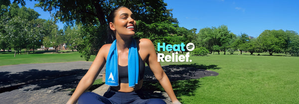 A smiling woman in athletic wear with a blue Alphacool towel around her neck sits in a sunny park. Text: Heat Relief.