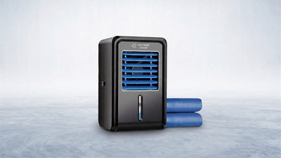 A sleek black mattress cooler with blue vents, a visible water level, and two blue cooling tubes extending to the right, on a light grey surface.