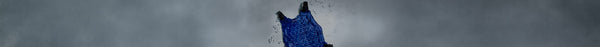 A textured, dark blue object with black straps stands vertically against an overcast grey sky, surrounded by small, scattered clear fragments.