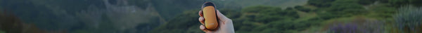 A hand holds an orange and black oval device with 