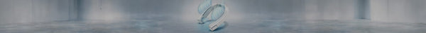 A white, S-shaped personal cooling device emits blue airflow, resting on a light grey floor in a clean, minimalist setting.
