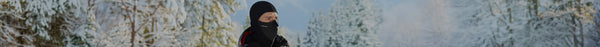 A person in a black balaclava and winter jacket looks right, surrounded by snow-covered trees in a serene winter forest.