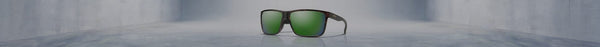Smith sunglasses with dark frames and vibrant green reflective lenses sit centered on a glossy grey floor in an empty, wide concrete room.