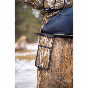 Person sitting on a Mobile Warming heated camo seat cushion on a tree stump