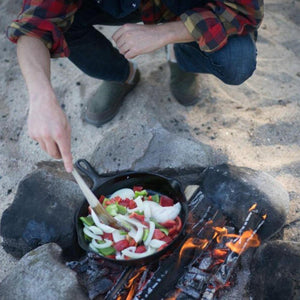 Person wearing Acorn shoes cooking vegetables in a cast iron skillet over a campfire