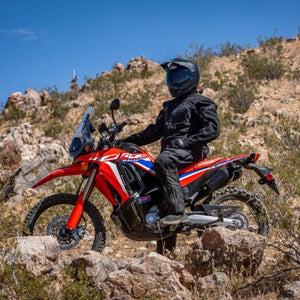 Motorcyclist wearing Tourmaster black riding gear on a red Honda rally bike on a rocky desert trail